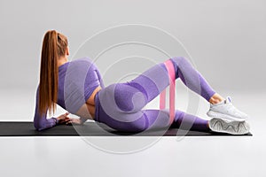 Fitness woman doing clamshell exercise for glutes with resistance band on gray background. Athletic girl working out photo