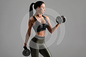 Fitness woman doing exercise for biceps on gray background. Muscular woman workout with dumbbells