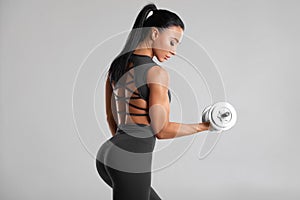 Fitness woman doing exercise for biceps on gray background. Muscular woman workout with dumbbells photo