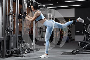 Fitness woman doing exercise for glutes, cable kickbacks. Athletic girl workout at the gym. Beautiful butt in leggings