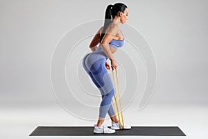 Fitness woman doing exercise with resistance band on gray background. Athletic girl working out