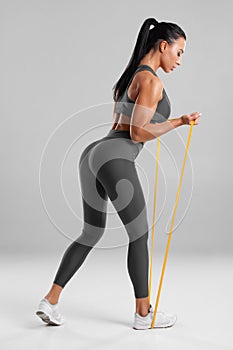 Fitness woman doing exercise with resistance band on gray background. Athletic girl working out