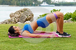 Fitness woman doing glute bridge exercise with resistance band, outdoors. Athletic girl workout