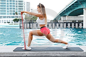 Fitness woman doing lunges exercises for leg muscle workout training with resistance band outdoors