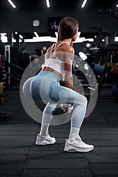 Fitness woman doing squat exercise for glutes in gym. Athletic girl working out with dumbbell