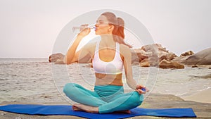 Fitness woman drink water after doing sport exercises on beach at sunset.