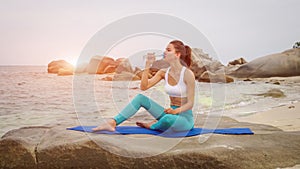 Fitness woman drink water after doing sport exercises on beach at sunset.