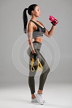 Fitness woman drinking water from a bottle, isolated on gray background. Active girl quenches thirst photo