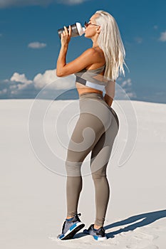Fitness woman drinking water, outdoor. Athletic girl quenches thirst. Beautiful female in leggings with sexy butt photo