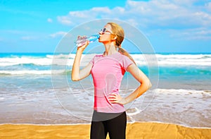 Fitness woman drinks water from bottle on the beach
