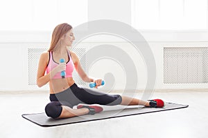 Fitness woman with dumbbells sitting on mat