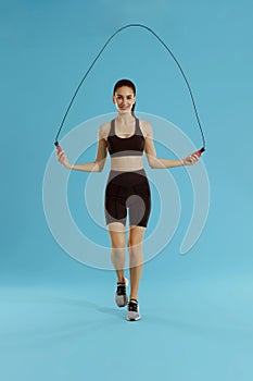 Fitness. Woman exercising with jumping rope on blue background