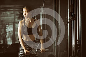 Fitness woman flexing arm muscles on cable machine at fitness center.