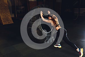 Fitness woman flipping wheel tire in gym. Fit female athlete working out with a huge tire. Back view. Sportswoman doing