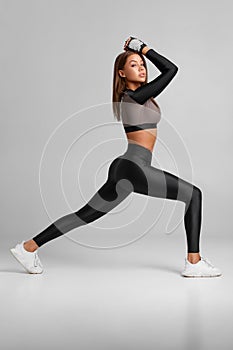 Fitness woman on gray background. Athletic girl doing lunges exercises for leg muscle training