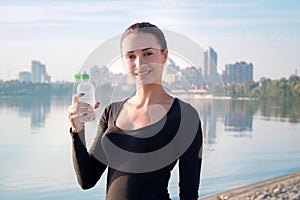 Fitness woman holds water bottle at river and city backround