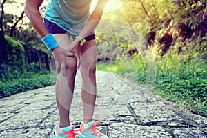 Fitness woman jogger hold her sports injured leg at forest trail