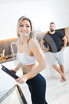 Fitness woman in kitchen, man in background. Husband and wife cooking together