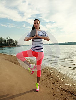 Fitness woman making yoga exercises on sand beach of river