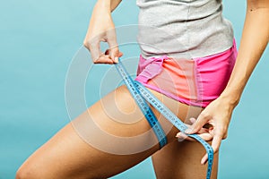 Fitness woman measuring her thigh on blue