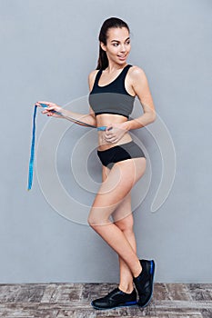 Fitness woman with measuring tape over grey background