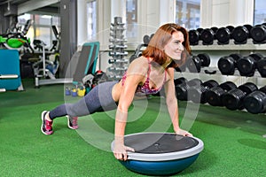 Fitness woman planking doing the body weight exercise for core strength training in gym with bosu balance trainer