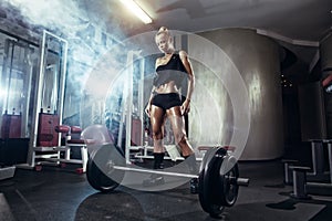 Fitness woman prepares for exercising with barbell in gym