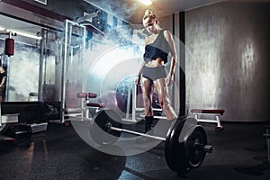 Fitness woman prepares for exercising with barbell in gym