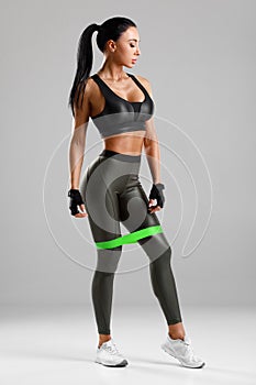 Fitness woman with resistance band on the gray background. Sporty girl
