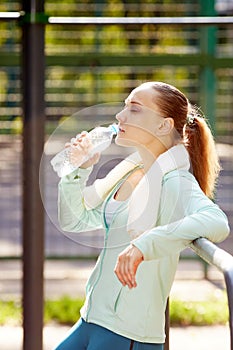 Fitness woman resting after workout, relaxing, drinking clear water from bottle outdoor fitness area in a park