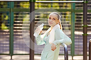 Fitness woman resting after workout, relaxing, drinking clear water from bottle outdoor fitness area in a park