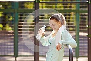 Fitness woman resting after workout, relaxing, drinking clear water from bottle outdoor fitness area in a park