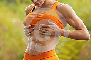 Fitness woman showing abs and flat belly. Athletic girl outdoors, shaped abdominal, slim waist