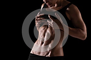 Fitness woman showing abs and flat belly, isolated on the black background. Sporty girl shaped abdominal