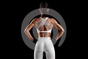 Fitness woman showing back muscles on black background. Athletic girl rear view