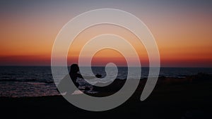 Fitness woman in silhouette doing squats exercises on beach near ocean. Young female in sportswear spending evening time