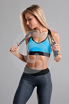 Fitness woman with skipping rope,  on gray background. Athletic girl workout, shaped abdominal