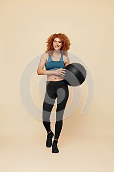 Fitness Woman. Smiling Redhead Girl Full-Length Portrait. Female In Sportswear And Sneakers Holding Fitness Ball.