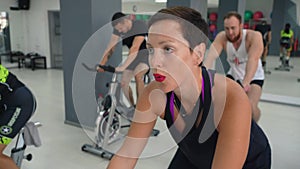 Fitness woman spinning static bike on cycling class in gym. Portrait sport woman breathing while cardio training in