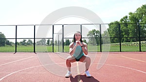 Fitness woman in sportswear doing various exercises on an orange basketball field with white markings, at the stadium