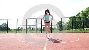 Fitness woman in sportswear doing various exercises on an orange basketball field with white markings, at the stadium