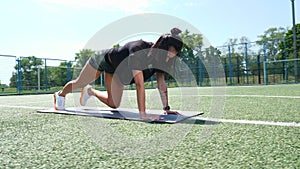Fitness woman in sportswear doing various exercises on sports mat, on green football field with white markings, at