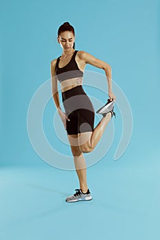 Fitness. Woman in sportswear stretching legs on blue background