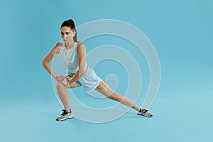 Fitness. Woman in sportswear stretching legs on blue background