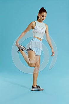 Fitness. Woman in sportswear stretching legs on blue background