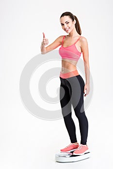 Fitness woman standing on weighing scale and showing thumbs up