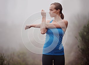 Fitness, woman and stretching arms outdoor, wellness or sports with fog. Park, serious and young person warm up in