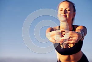 Fitness woman stretching hands on blue sky background. She does exercises after running. healthy lifestyle concept