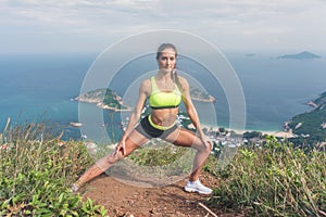 Fitness woman stretching her leg muscles doing side lunge exercise preparing for cardio work-out in mountains by the sea
