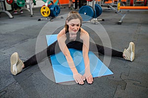 Fitness Woman stretching legs sitting on gym mat. Sport and healthy lifestyle.